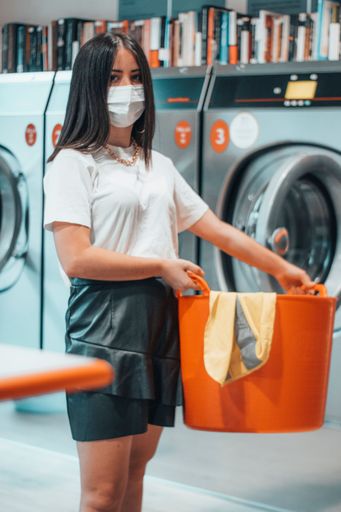 A shallow focus shot of a young caucasian brunette girl standing with an orange laundry basket in her hands