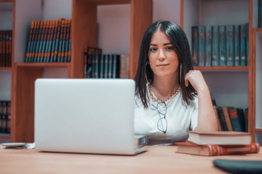 A shallow focus shot of a young smiling brunette caucasian girl studying in a library with a laptop