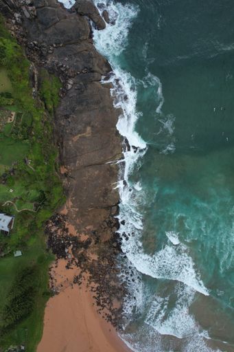 A vertical top view of sea waves crashing on a rocky shore