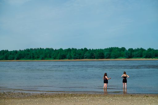 Two women standing next to a tranquil lake with green trees in the background