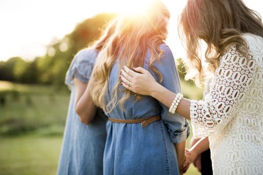 A closeup shot of females with their arms on each other while praying with a blurred background