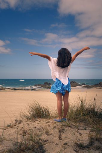 A vertical shot of a young female standing on a sandy beach with her arms stretched against the sea