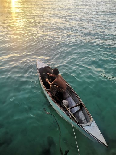 A vertical shot of a boy in the boat during the sunset