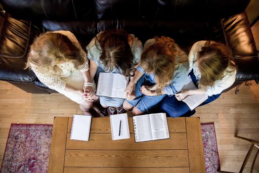 An overhead shot of females sitting while holding hands and reading the bible