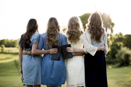 A beautiful shot of female with their arms around each other while holding the bible