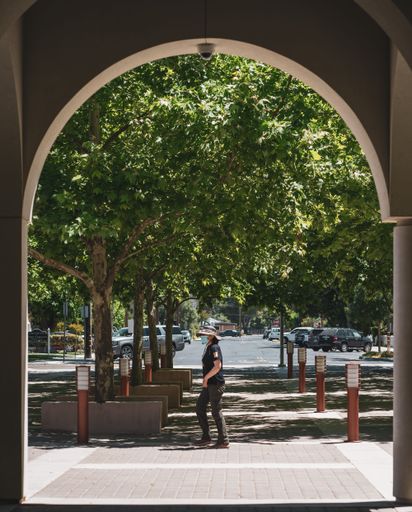 A vertical shot through the arch of a female with a mask walking in a park