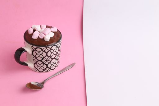 A high angle shot of a cup full of hot chocolate and marshmallows on with a spoon placed next to it