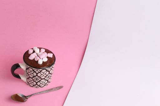 A high angle shot of a cup of hot chocolate with marshmallows on a pink and white surface
