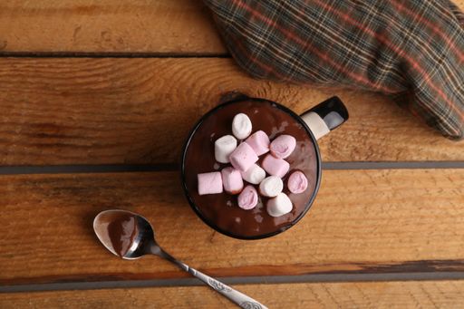 A closeup shot of a cup of melted chocolate and sweet marshmallows on top