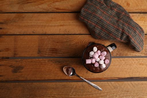 A high angle shot of a cup of hot chocolate with marshmallows and a spoon on a wooden surface