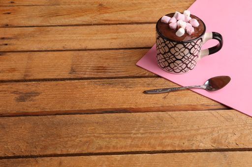 A high angle shot of a cup of melted chocolate with marshmallows on a pink paper on a wooden surface