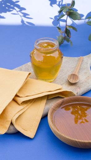 A vertical of honey in a glass jar on a blue background.