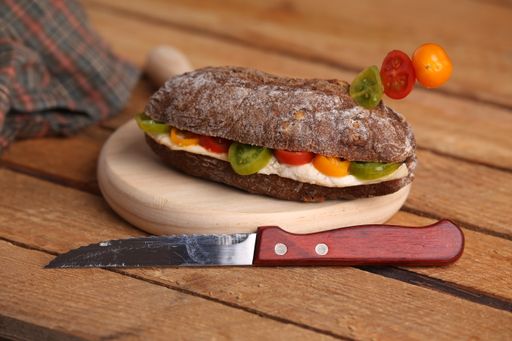 A closeup shot of a chicken breast sandwich with tomatoes on walnut bread on a wooden surface