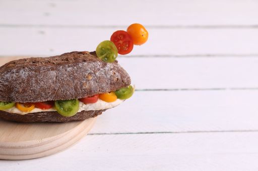 A closeup of a sandwich with cherry tomatoes and chicken breast in the middle on a round wooden board