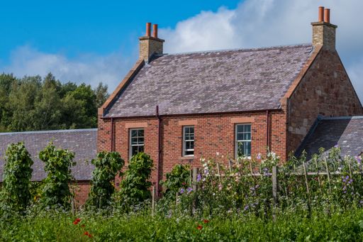 A brown brick house in a green area under the bright sunlight