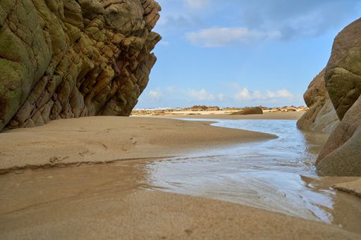 A beautiful view of a coastline surrounded by large rocks under a cloudy blue sky