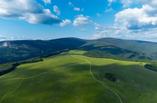 An aerial view of a wavy green mountain plain under blue cloudy sky on a sunny day