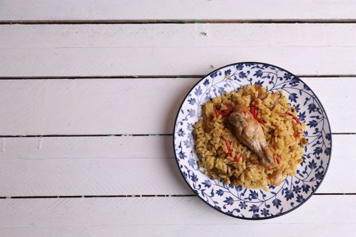 A top view of a plate of curried rice topped with a chicken drumstick on a white wooden surface