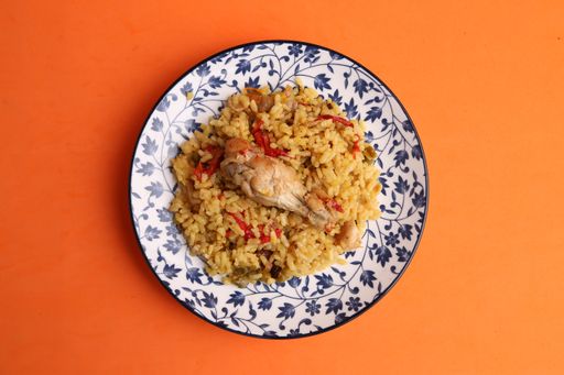 A closeup shot of a plate of rice with chicken and peppers on an orange background