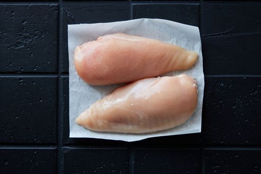 Top view of raw chicken breasts on napkin placed on black background in light kitchen during cooking preparation at home