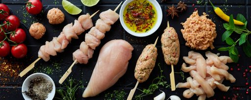 A top view of a mix of raw chicken breasts, strips, skewers, and Lula kebab on table with condiments
