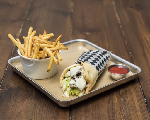 A closeup shot of a sandwich next to french fries on a wooden table