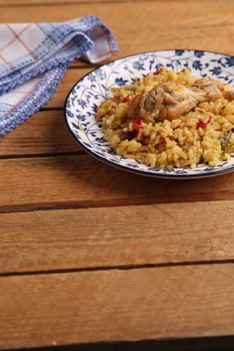 A vertical closeup of a plate of curried rice topped with a chicken drumstick on a wooden surface