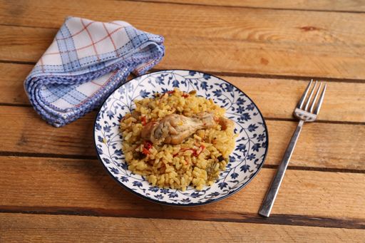 A high angle shot of a plate of chicken and rice and a spoon isolated on a wooden surface