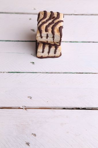 A vertical closeup of two stacked chocolate drizzled biscuits on a white wooden surface