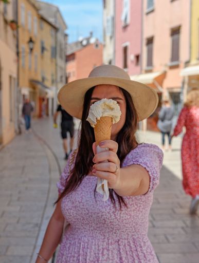 A Caucasian woman in pink dress holding the ice-cream in front of her face toward the camera