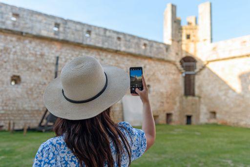 A back view of Caucasian woman taking photo of medieval castle through phone