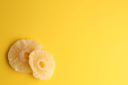 An overhead shot of dried pineapple slices on a yellow background