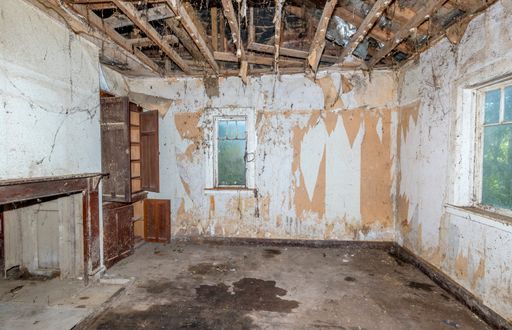 a dangerous and unsanitary living room of an abandoned house with ceiling missing, exposed wiring, cobwebs and puddled water on the floor