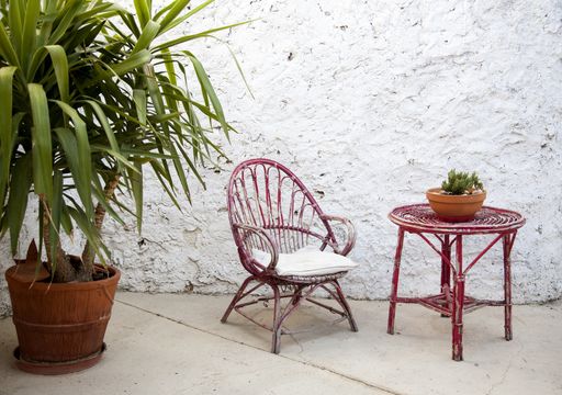 A pink chair, table, and a potted palm tree in front of a white grunge wall