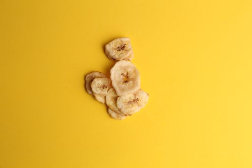 A top view closeup of nutritious dried banana chips on a yellow surface