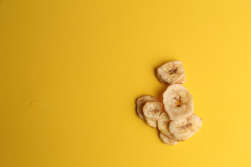 A flat lay shot of dry banana chips on a yellow surface