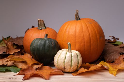 A closeup shot of pumpkins surrounded by leaves on a wooden surface getting ready for Halloween