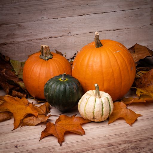 A high angle shot of pumpkins surrounded by leaves on a wooden surface getting ready for Halloween