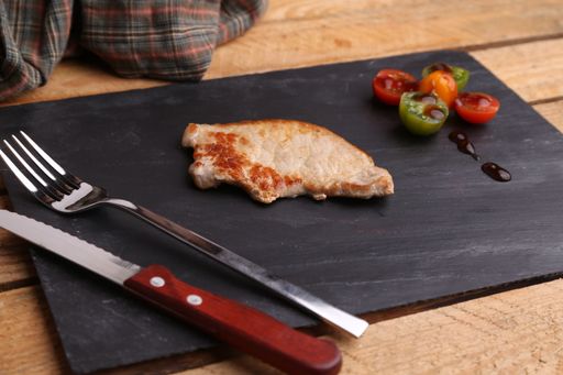 A high angle shot of fried chicken and some tomatoes on a black plate on a wooden surface