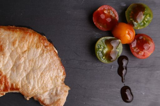 A high angle shot of a piece of fried chicken and some tomatoes isolated on a black surface