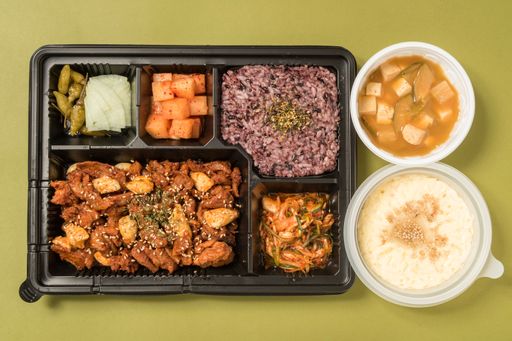 a flat lay of a tray with a variety of Asian food isolated on a green background.