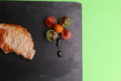 A pork tenderloin steak with tomatoes on green tray
