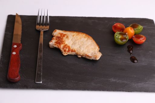 A closeup shot of a steak with grilled vegetables on a black chopping board