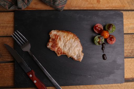 A top view of a pork chop steak next to fork and knife