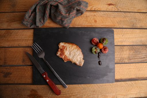 A high angle shot of the delicious and juicy ribeye  steak with sliced tomatoes on the wooden board