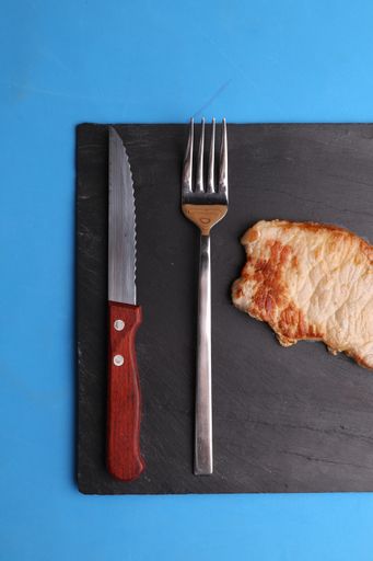 A closeup of the delicious steak with a knife and fork isolated on a blue background
