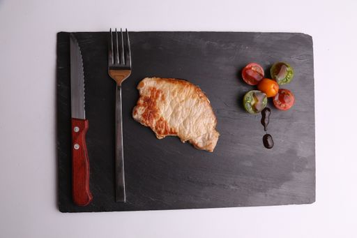 A closeup shot of a steak with grilled vegetables on a black chopping board