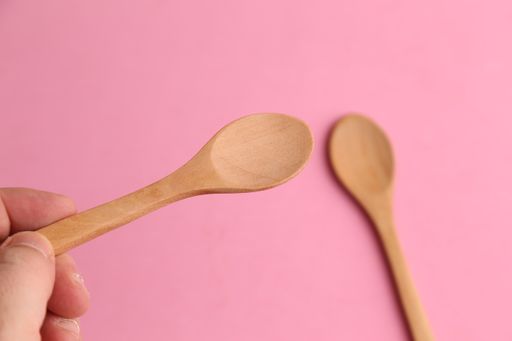 A top view of a person holding a small wooden spoon with a pink blurry background