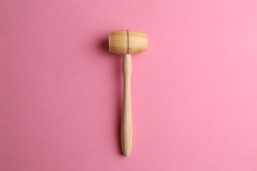 An overhead shot of a wooden hammer isolated on a pink background
