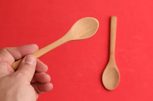 An overhead shot of a male hand holding a wooden spoon on a red background